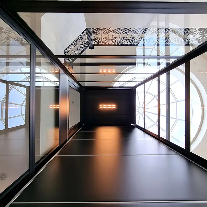 Standing inside the Compact Home Lift, looking upwards in the lift shaft that is steel framed with glass panels, the dark shaft ceiling has LCD lights 