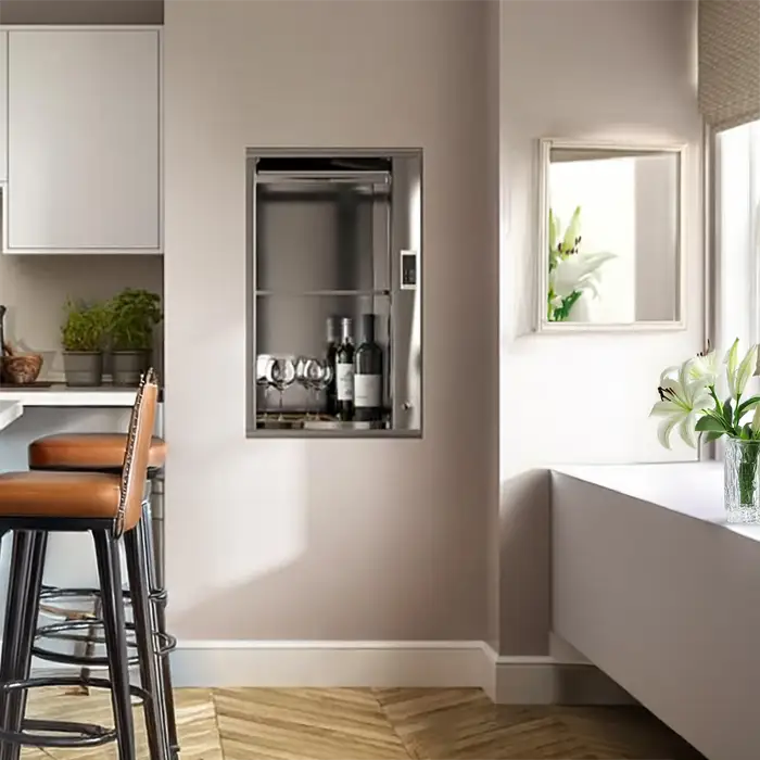 A kitchen setting with a dumb witer installed in the far wall. The lift doors are open and inside are two bottles of wine and two glasses