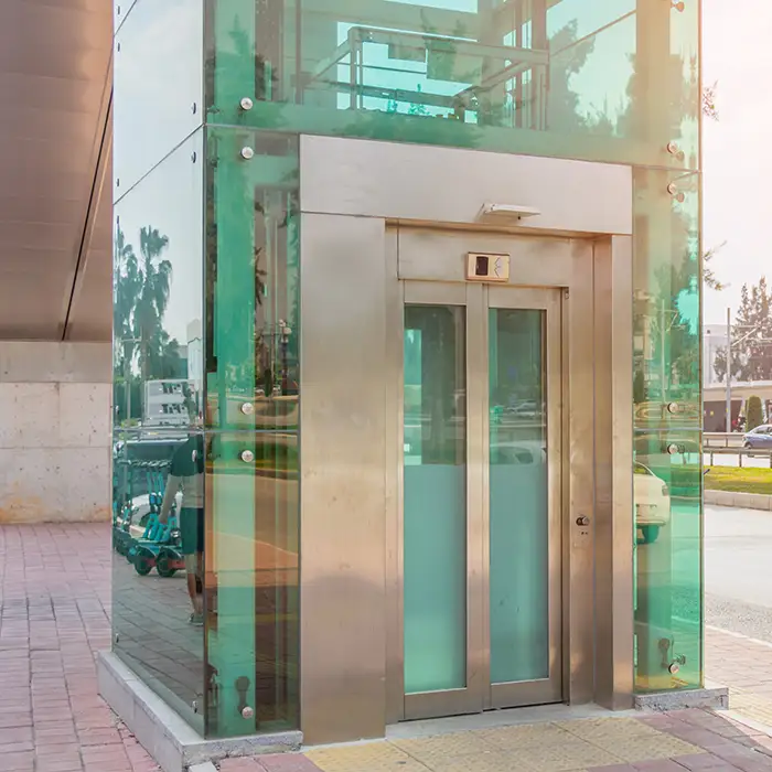 A steel lift elevator structure with pinned glass and stainless steel telescopic doors installed outside near a busy road