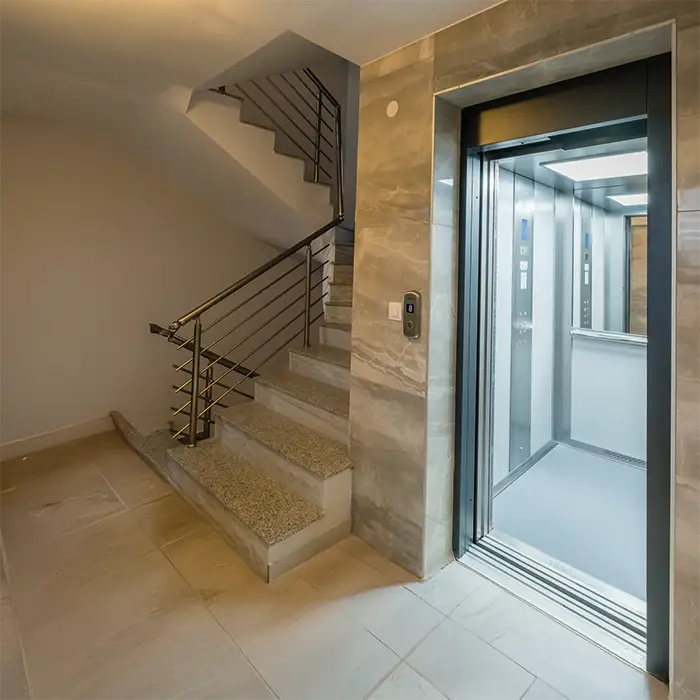 The passenger lift telescopic doors are open on the landing of a commercial stairwell, inside you can see the mirrored wall with a handrail of the lift cabin and the controls of the elevator on the left