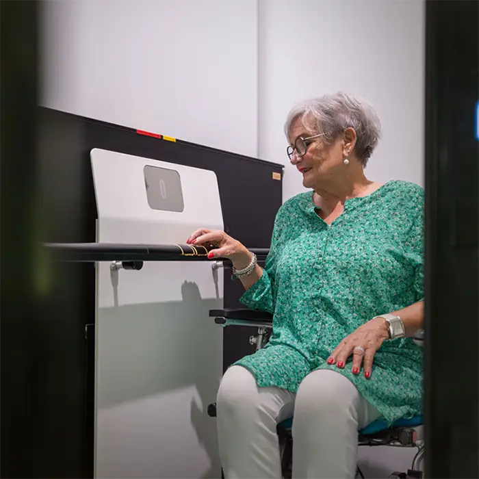 A lady wheelchair user wearing a green top sat in her wheelchair inside the wheelchair lift. Her right hand is resting on the controls and the elevator door is open.